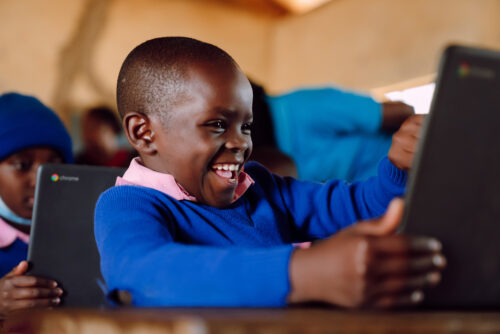 A Kenyan child smiles at a computer.