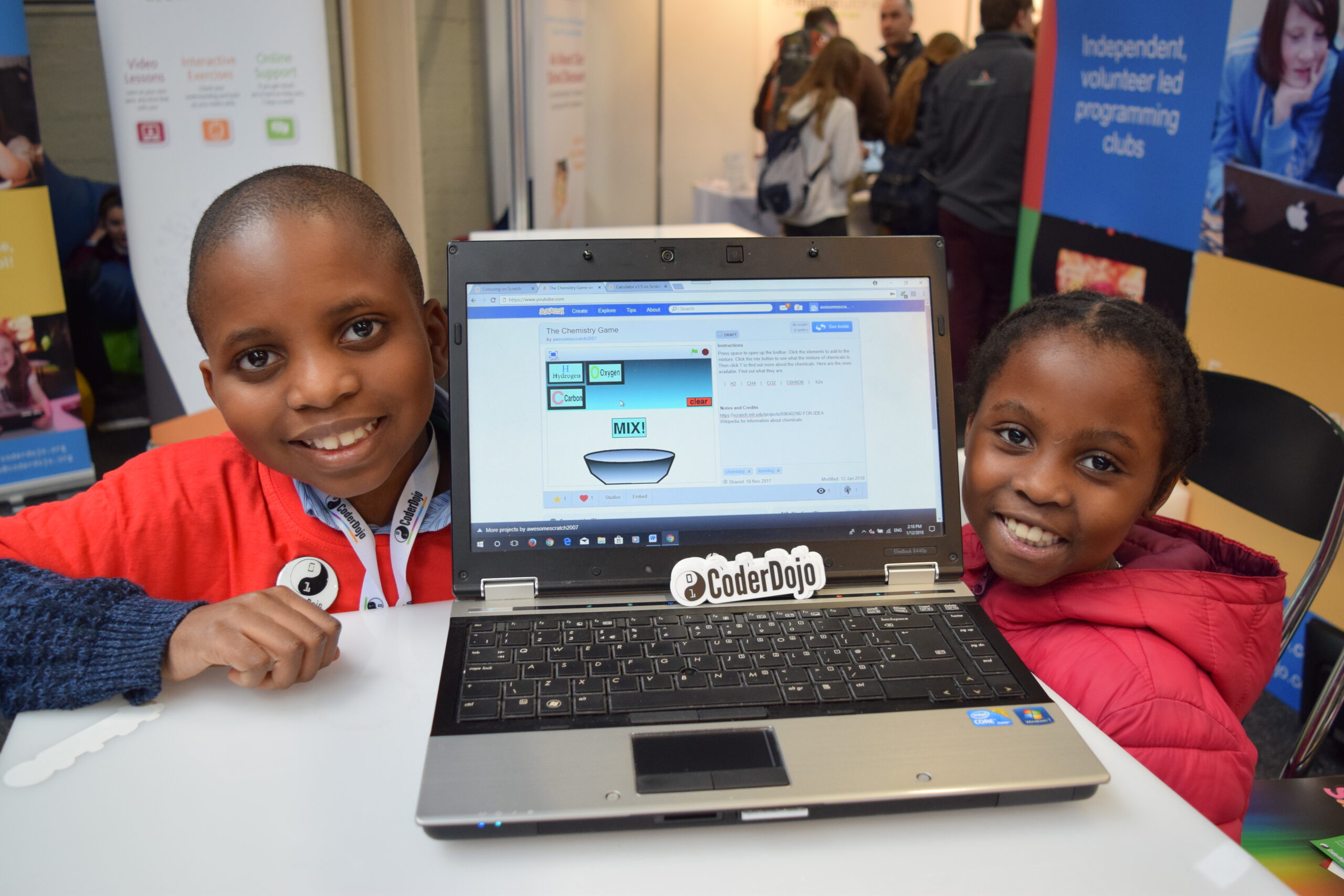 A brother and sister show off their coding project on a laptop.