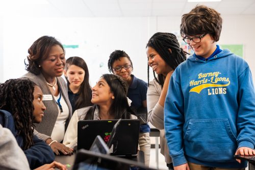 A group of young people and educators smiling while engaging with a computer