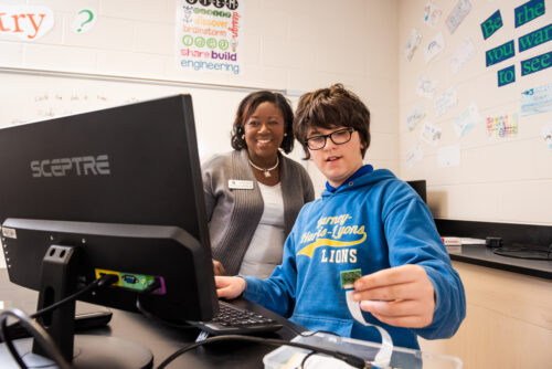 A teacher helps a young person with a coding project.