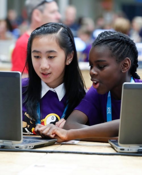 Two girls code at a laptop.