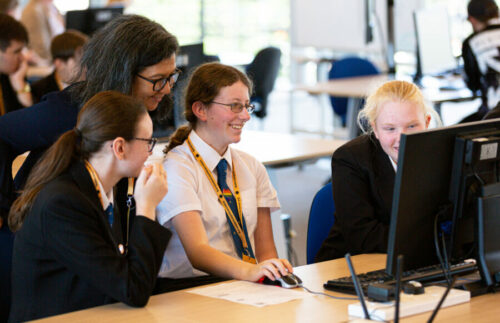 Three female teenagers and a teacher use a computer together.