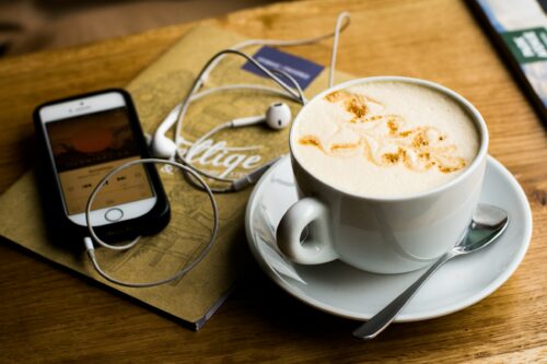 A phone with headphones plugged in next to a cup of coffee on a table.