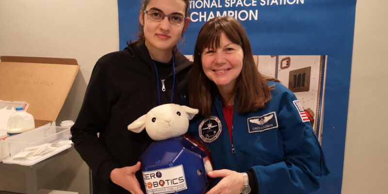 A teenage girl and NASA astronaut Catherine Grace Coleman hold a robot with a toy sheep's head.
