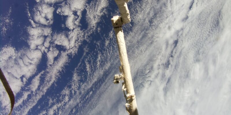 The earth’s surface from the perspective of the International Space Station, with a large robotic arm in view.