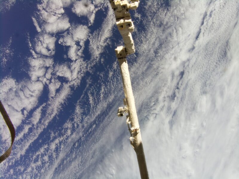 The earth’s surface from the perspective of the International Space Station, with a large robotic arm in view.