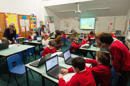 A class of primary school students do coding at laptops.