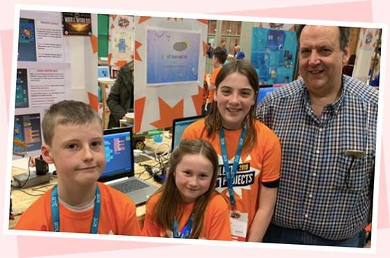 Three children and an adult standing in front of a coding stand