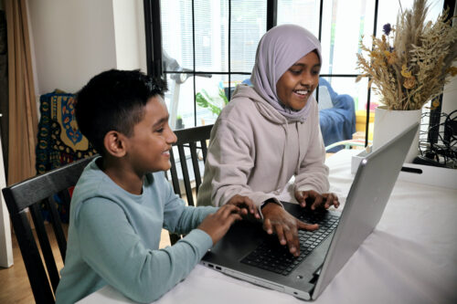 A sister and brother smiling while doing digital making at a laptop